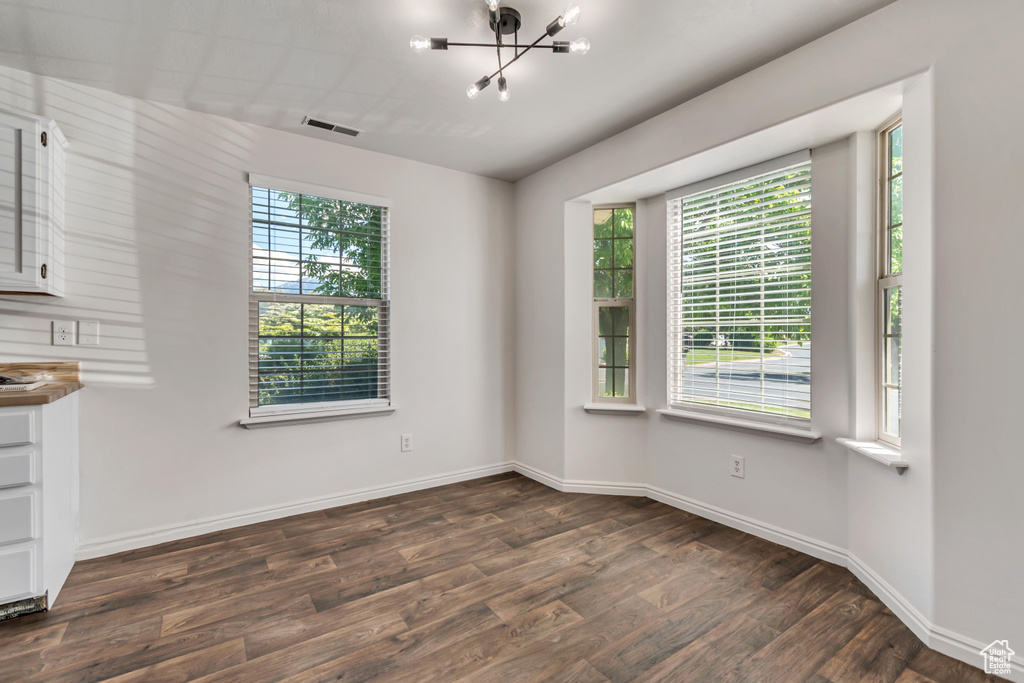Unfurnished dining area with dark wood-style floors, a chandelier, and baseboards