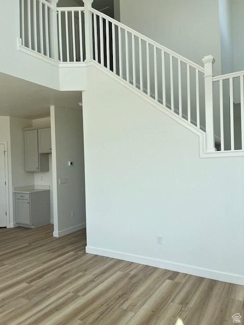 Unfurnished living room featuring light wood-style flooring, a towering ceiling, and stairs