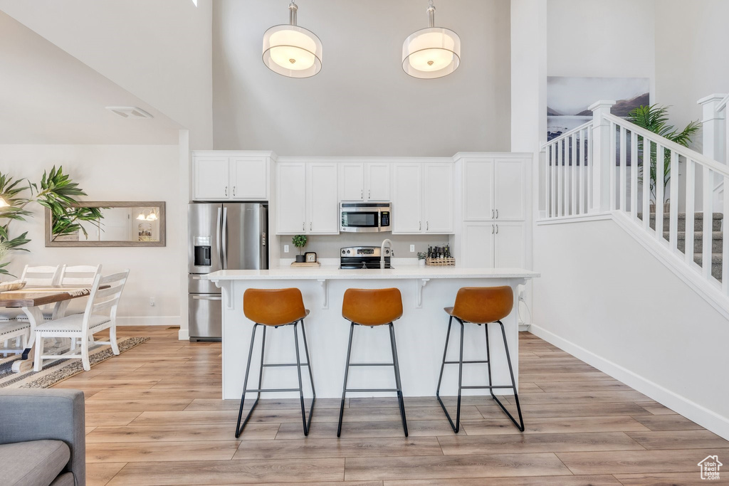 Kitchen with stainless steel appliances, a towering ceiling, a kitchen bar, white cabinetry, and light countertops