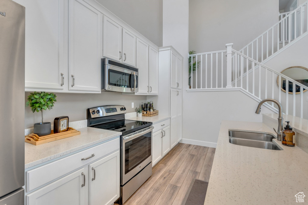 Kitchen with stainless steel appliances, a sink, light wood-style flooring, light stone countertops, and white cabinets