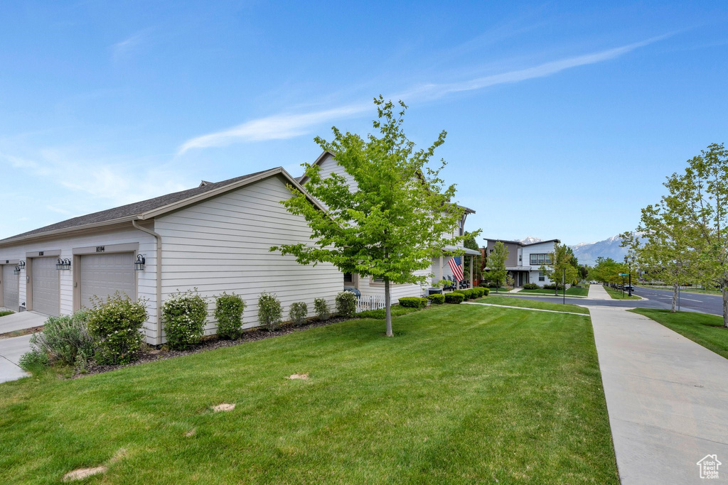 View of side of home with a yard, an attached garage, a mountain view, and driveway