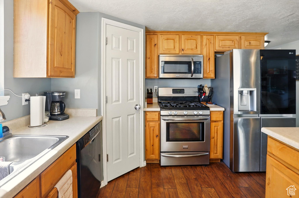 Kitchen featuring stainless steel appliances, light countertops, dark wood-style flooring, a textured ceiling, and a sink