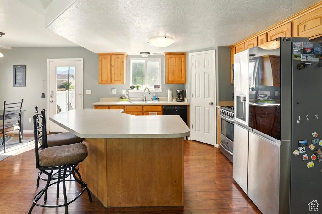 Kitchen featuring stainless steel appliances, light countertops, dark wood-style flooring, a sink, and a kitchen island