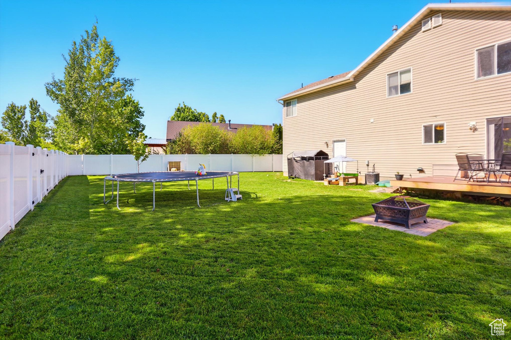 View of yard featuring an outdoor fire pit, a wooden deck, and a trampoline