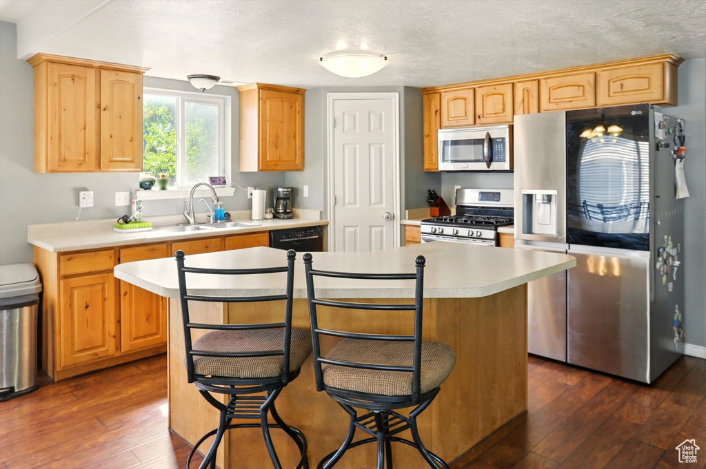 Kitchen featuring appliances with stainless steel finishes, a sink, light countertops, dark wood-type flooring, and a breakfast bar area