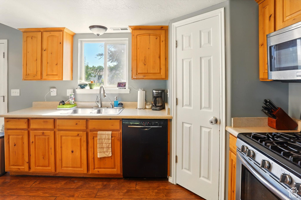 Kitchen featuring appliances with stainless steel finishes, a sink, light countertops, and dark wood-style floors