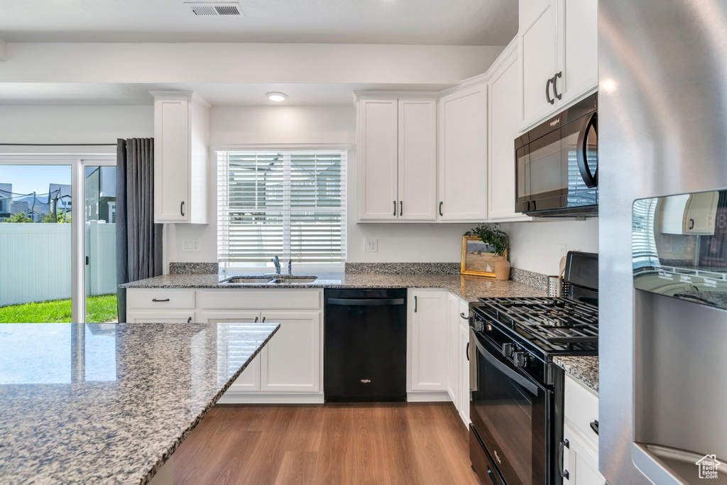 Kitchen with black appliances, wood finished floors, white cabinets, a sink, and light stone counters
