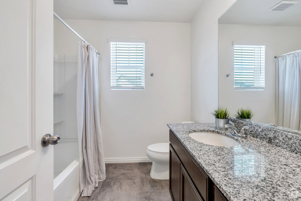 Bathroom featuring vanity, healthy amount of natural light, toilet, and shower / tub combo with curtain