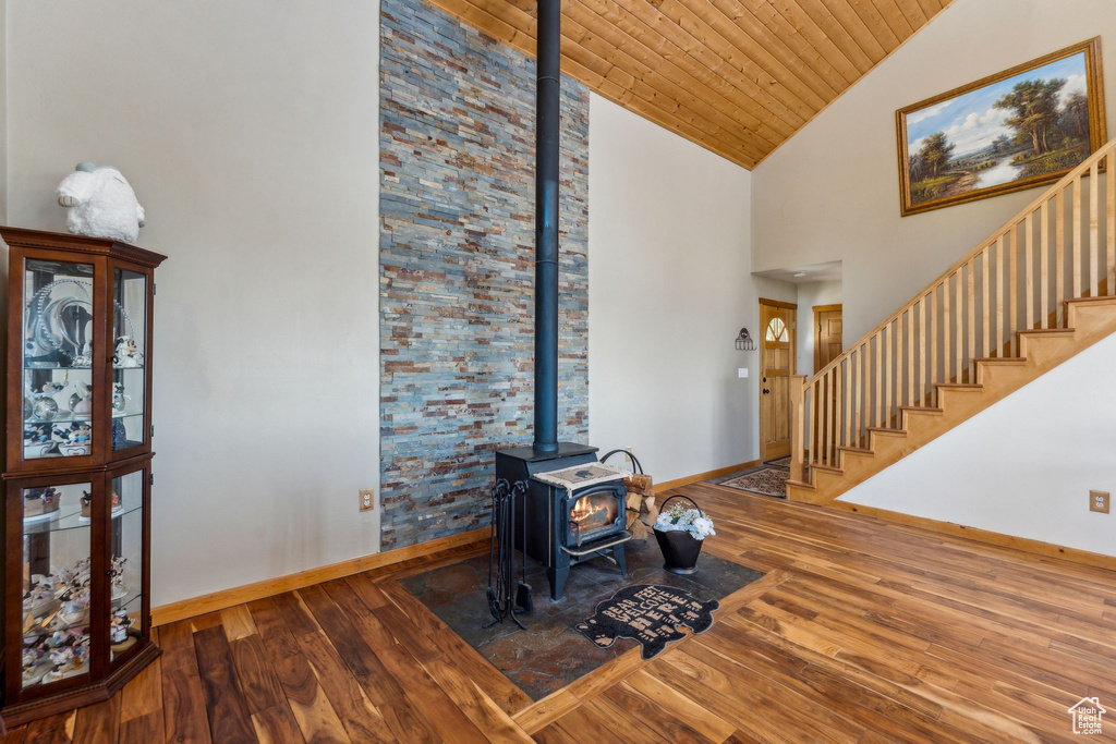 Living room featuring a wood stove, wood-type flooring, baseboards, high vaulted ceiling, and stairway
