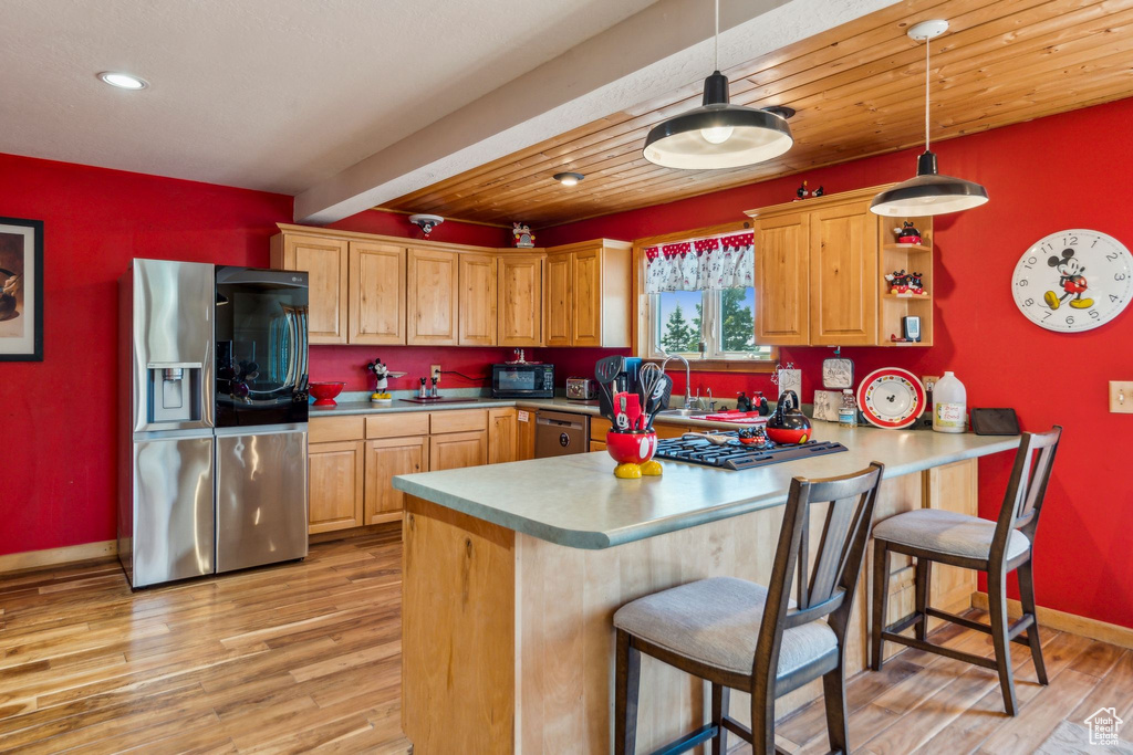 Kitchen featuring appliances with stainless steel finishes, light wood-style floors, baseboards, a peninsula, and pendant lighting