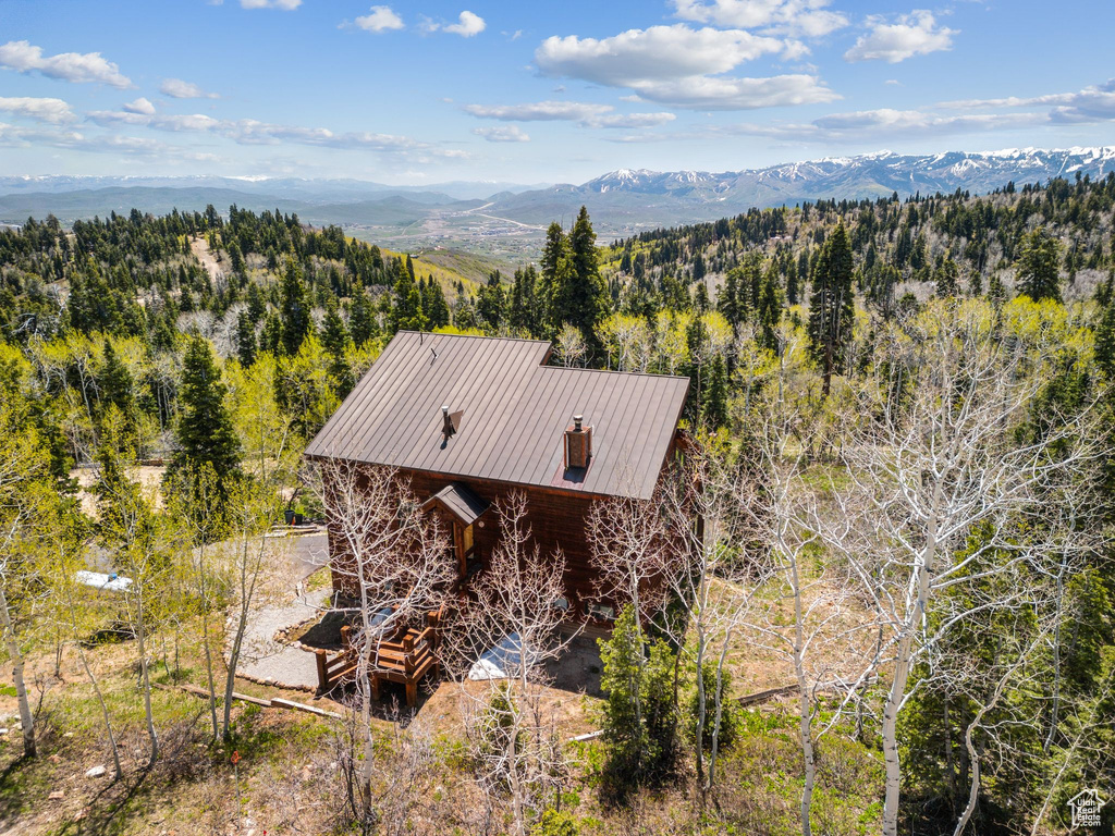 Aerial view of property and surrounding area featuring a mountain backdrop and a forest