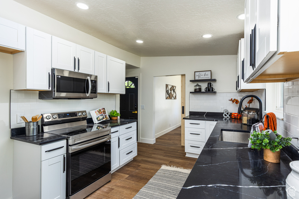 Kitchen with stainless steel appliances, a sink, tasteful backsplash, white cabinetry, and dark countertops