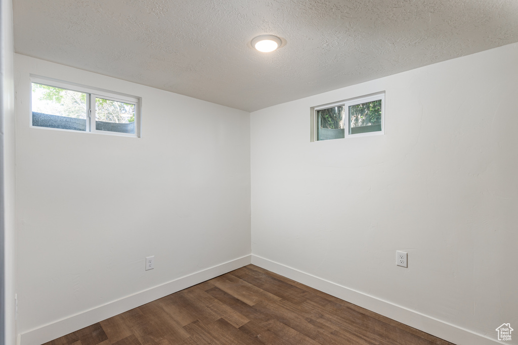Empty room featuring a textured ceiling, dark wood-style floors, and baseboards