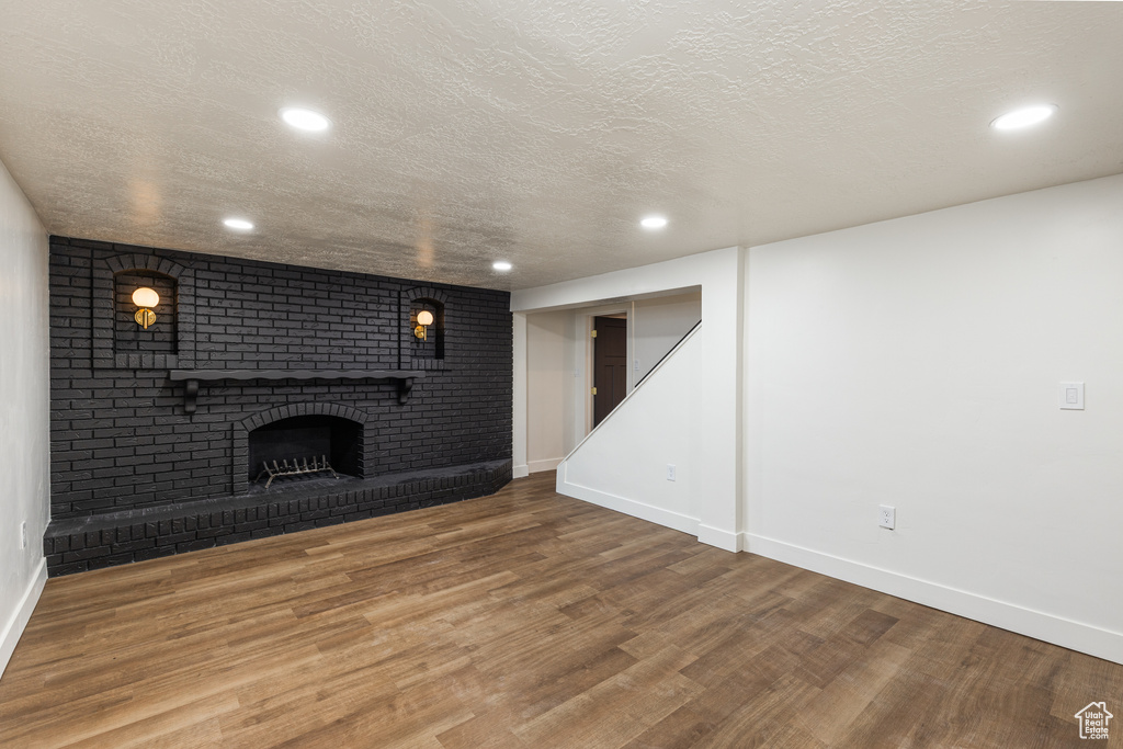 Unfurnished living room featuring a textured ceiling, wood finished floors, baseboards, a brick fireplace, and recessed lighting