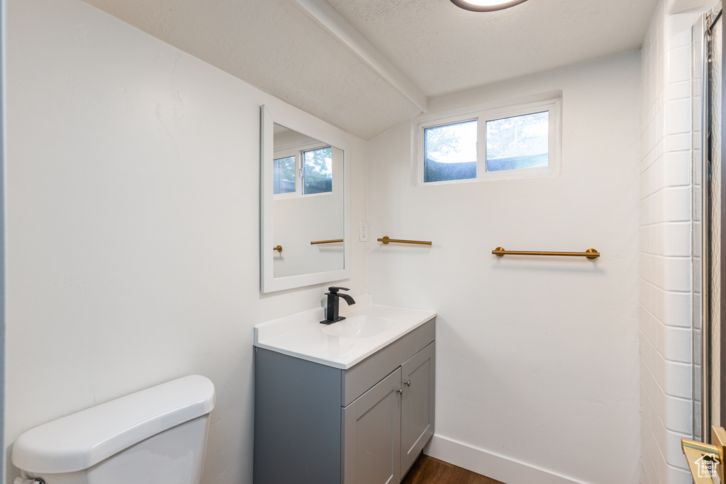 Full bath with toilet, vanity, vaulted ceiling, wood finished floors, and baseboards