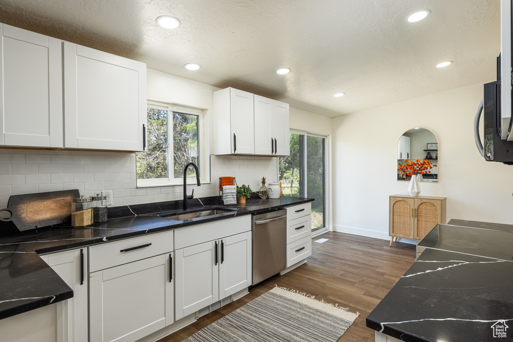 Kitchen featuring stainless steel dishwasher, a sink, decorative backsplash, dark wood finished floors, and white cabinets