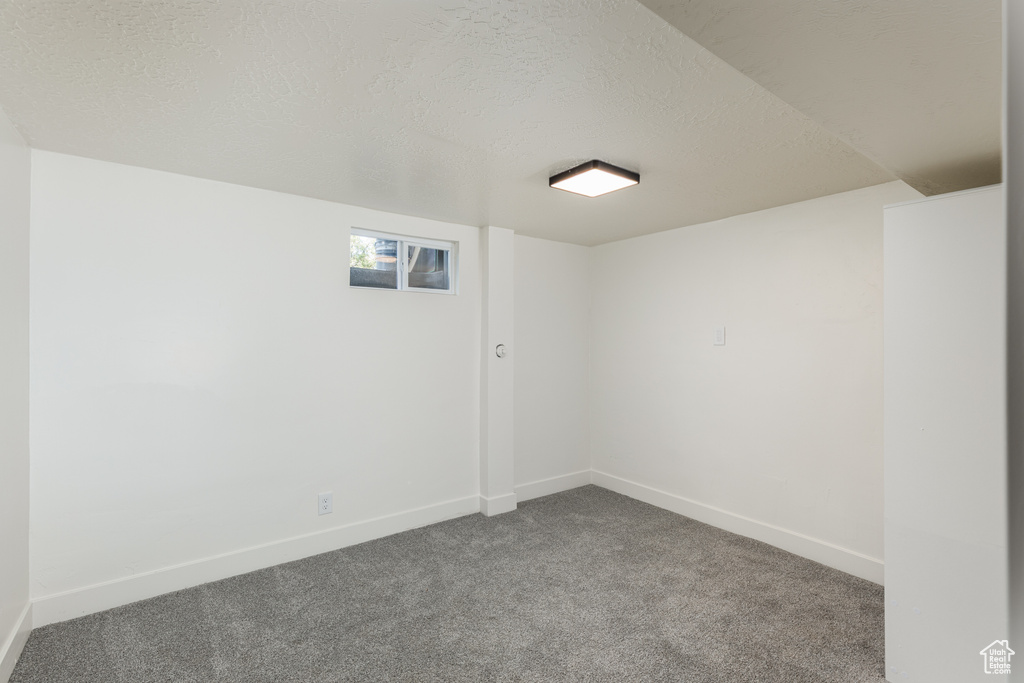 Unfurnished room with a textured ceiling, dark colored carpet, and baseboards
