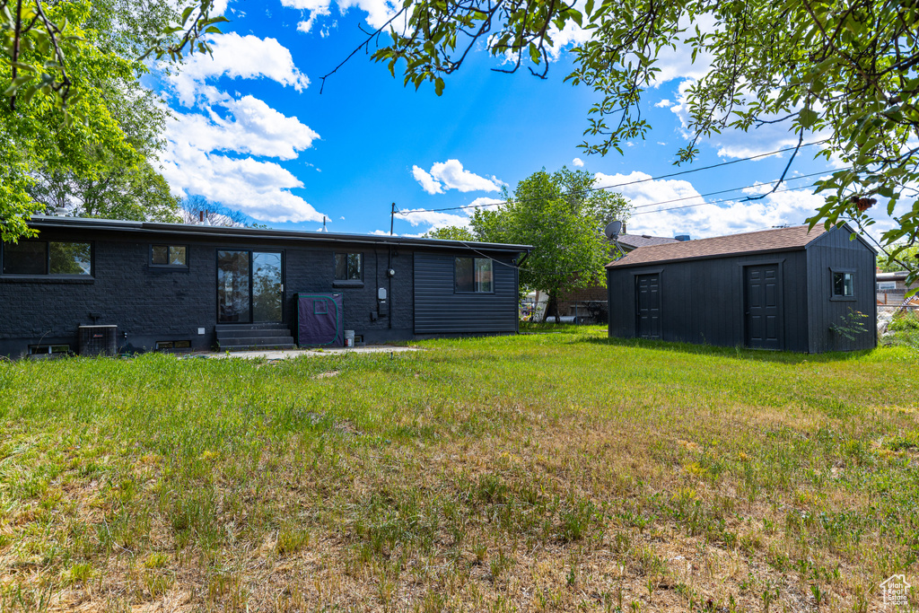 Rear view of house with an outdoor structure, a lawn, and entry steps