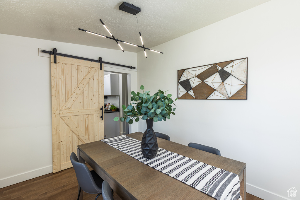 Dining room with baseboards, dark wood-style floors, a barn door, and a textured ceiling
