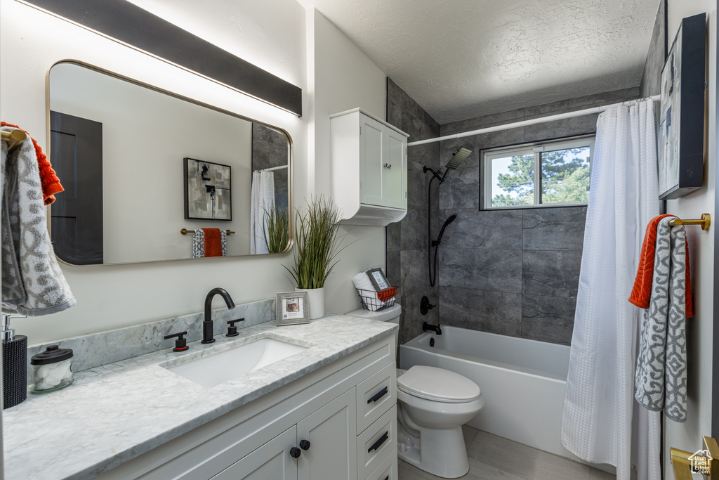 Bathroom with vanity, toilet, shower / bath combo with shower curtain, and a textured ceiling