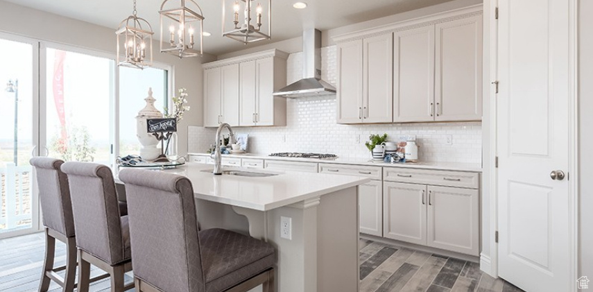 Kitchen with wall chimney range hood, a sink, plenty of natural light, a kitchen island with sink, and recessed lighting