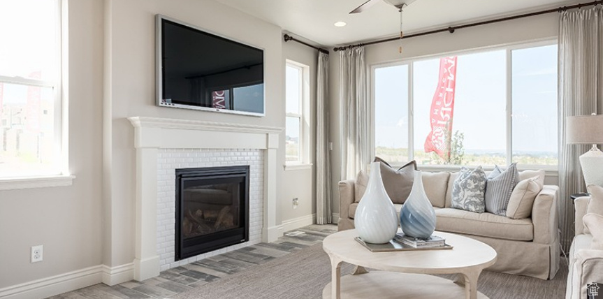 Living area with a glass covered fireplace, a ceiling fan, plenty of natural light, wood finished floors, and recessed lighting