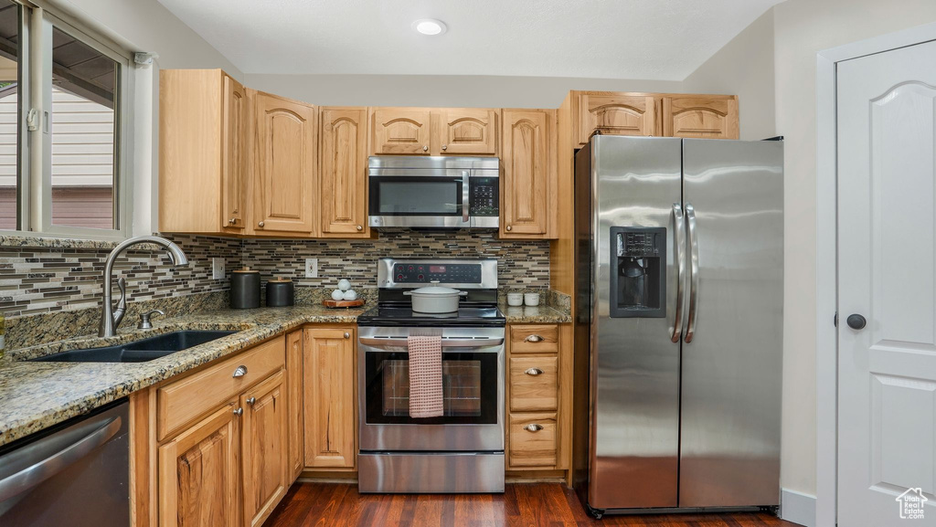 Kitchen featuring stainless steel appliances, a sink, light stone countertops, dark wood-style floors, and backsplash