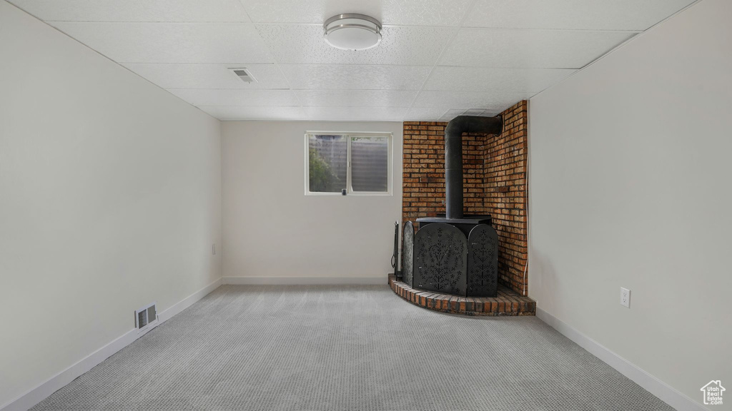 Unfurnished living room with a wood stove, carpet flooring, a paneled ceiling, and baseboards