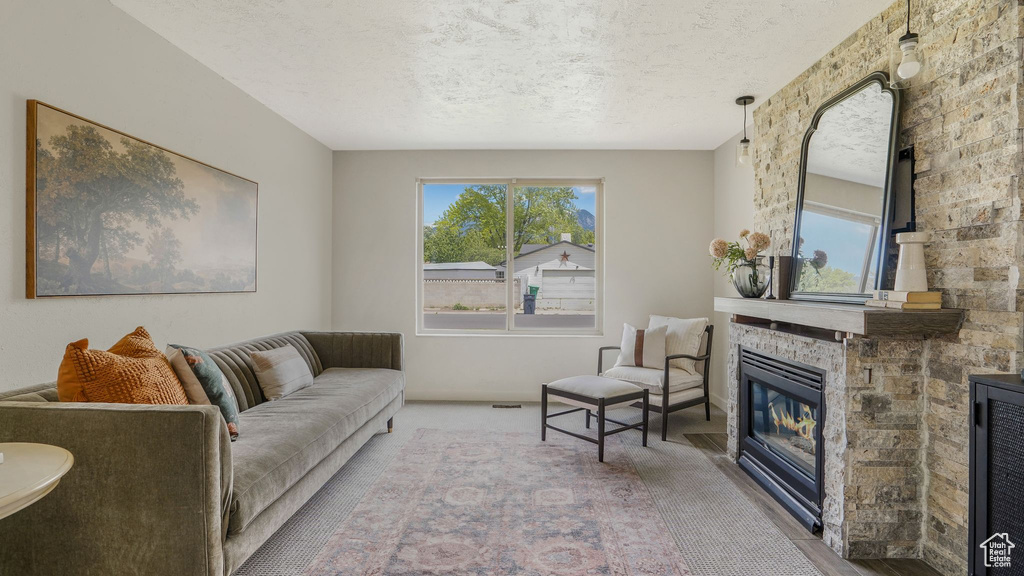 Carpeted living room featuring plenty of natural light, a textured ceiling, and a stone fireplace