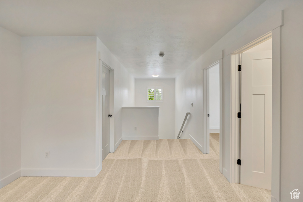 Hall with an upstairs landing, light colored carpet, and baseboards