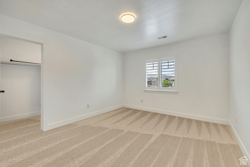 Unfurnished bedroom with light carpet, baseboards, and a walk in closet
