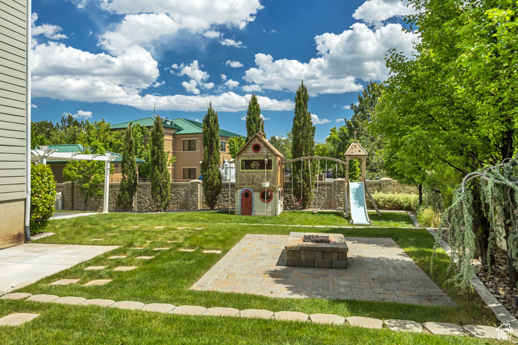 View of grassy yard with a playground, an outdoor fire pit, and a patio area