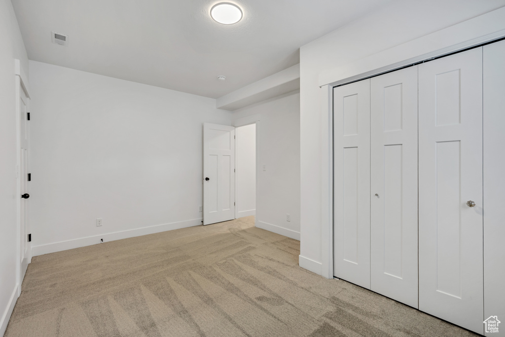 Unfurnished bedroom with light carpet, baseboards, and a closet