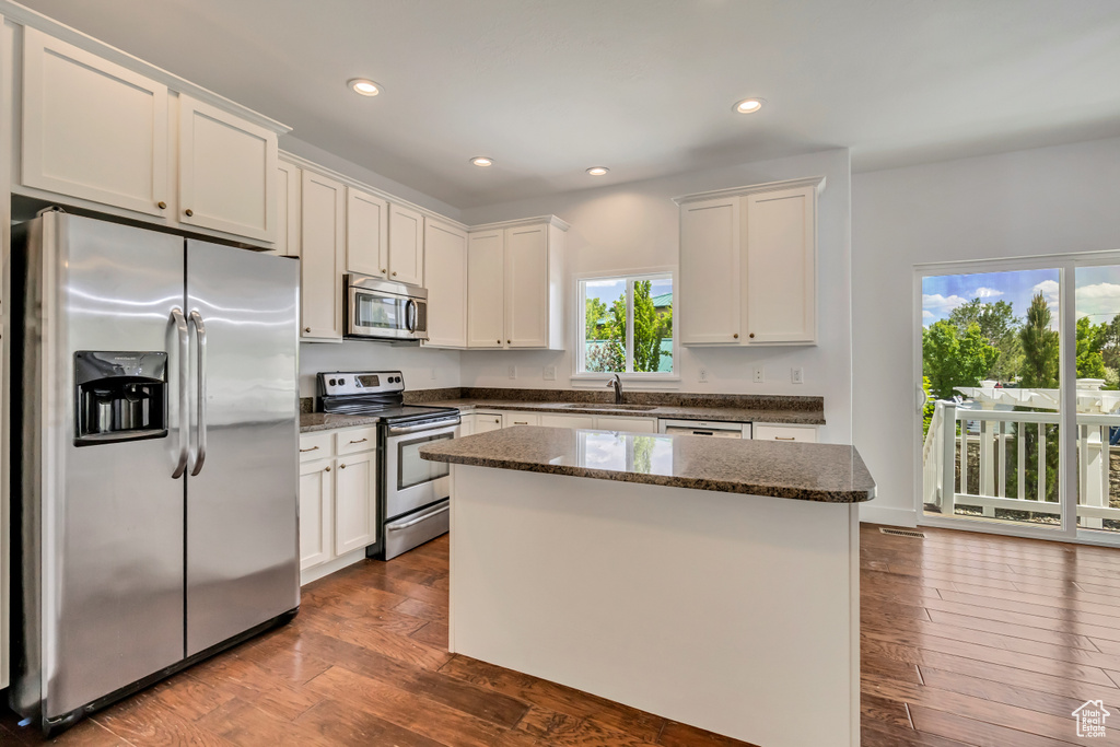 Kitchen featuring stainless steel appliances, a sink, a center island, white cabinetry, and dark wood finished floors