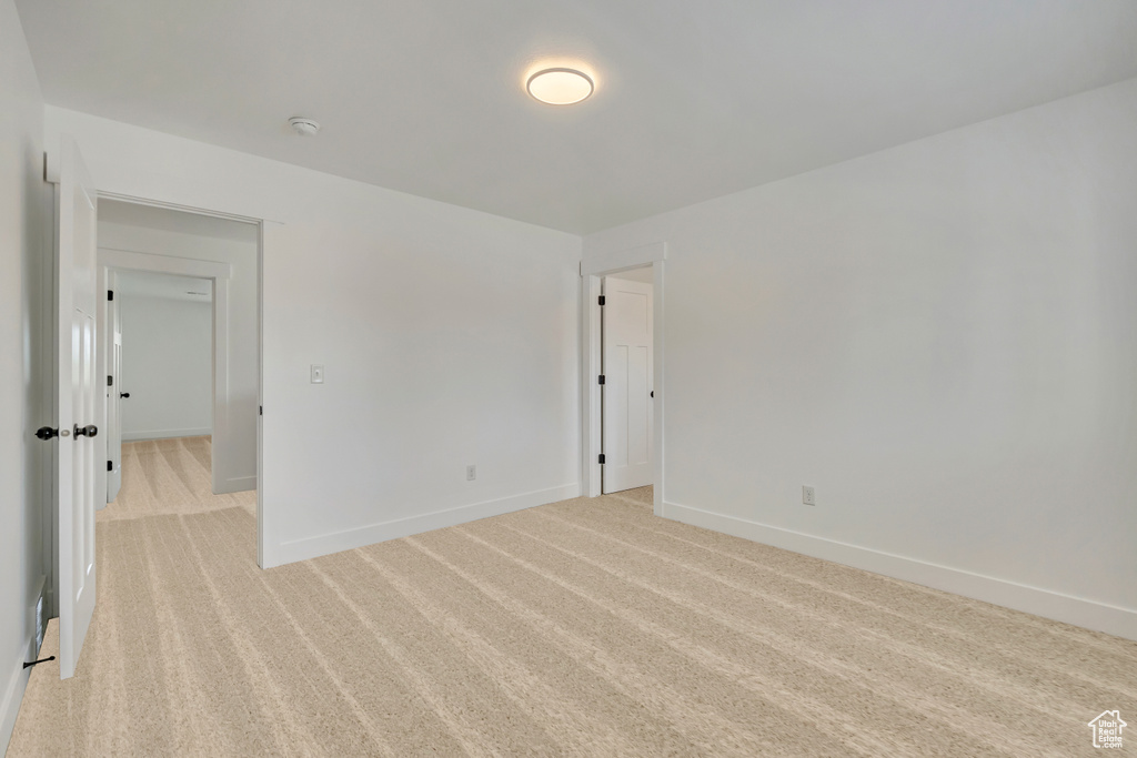 Empty room featuring light colored carpet, baseboards, and a smoke detector