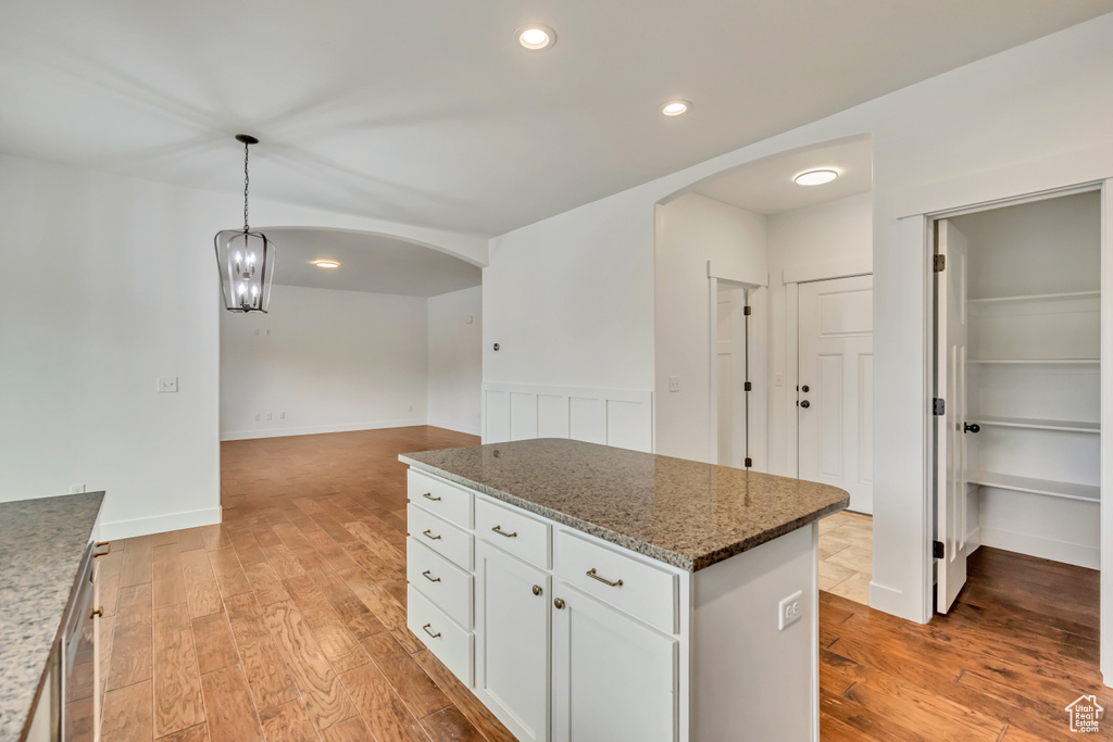 Kitchen with arched walkways, light wood finished floors, a center island, white cabinetry, and recessed lighting
