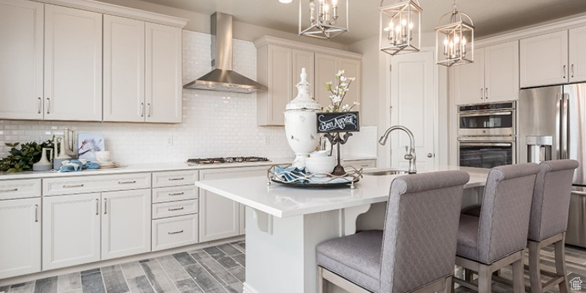Kitchen featuring appliances with stainless steel finishes, wall chimney range hood, a sink, light countertops, and a chandelier