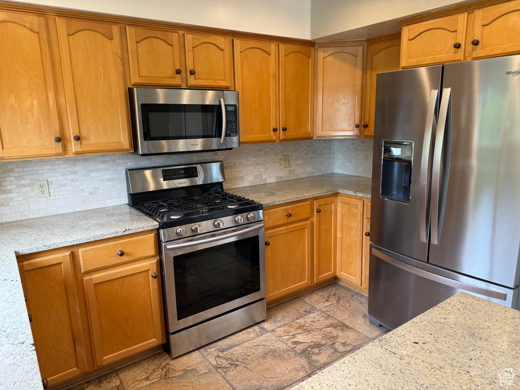 Kitchen with appliances with stainless steel finishes, backsplash, and brown cabinets