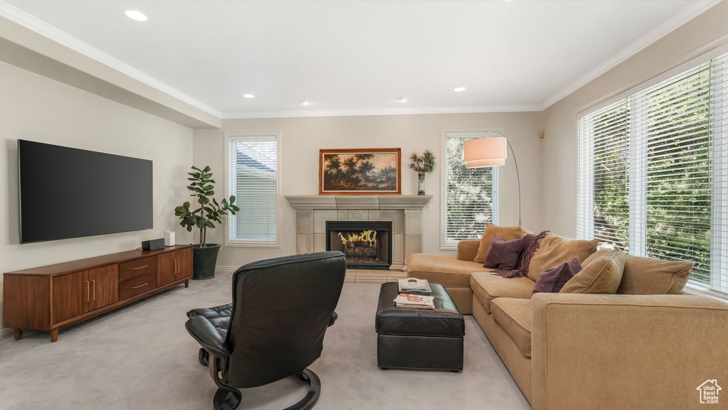 Living area featuring plenty of natural light, a tiled fireplace, light carpet, crown molding, and recessed lighting