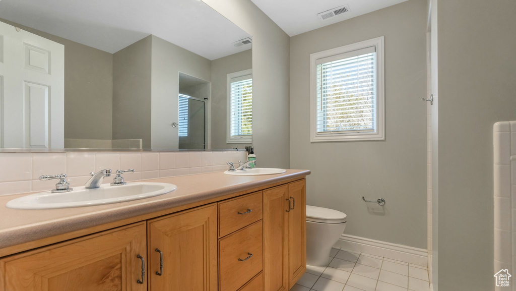 Bathroom with toilet, a shower stall, double vanity, baseboards, and tile patterned floors