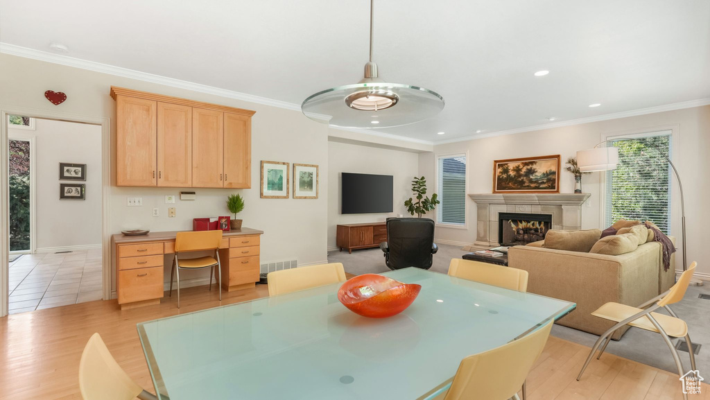 Dining room with a warm lit fireplace, light wood finished floors, a desk, baseboards, and ornamental molding