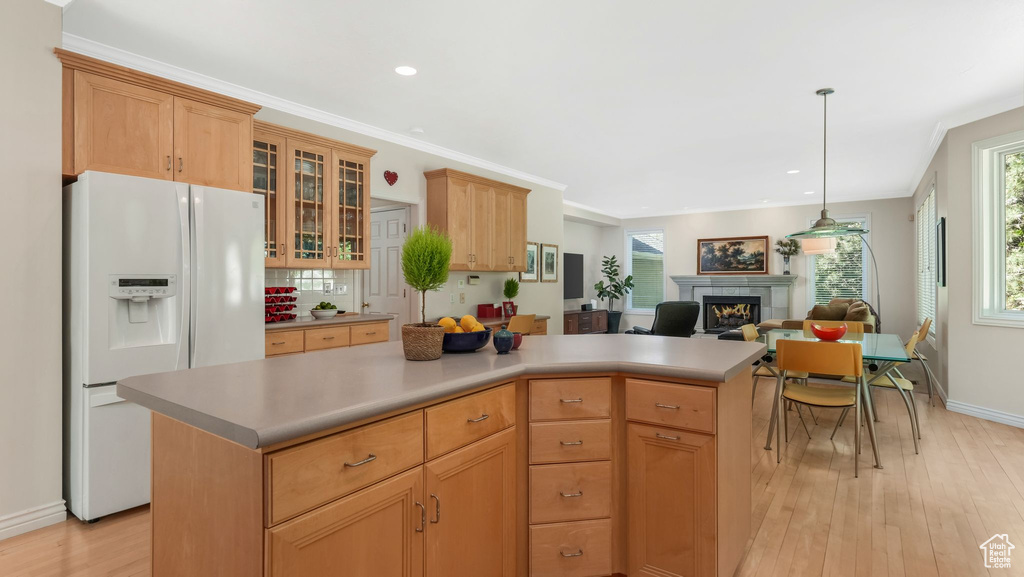 Kitchen with white fridge with ice dispenser, light wood-style flooring, a lit fireplace, glass insert cabinets, and plenty of natural light