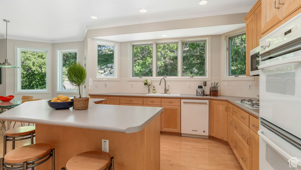 Kitchen featuring a sink, light brown cabinets, a kitchen breakfast bar, white appliances, and light countertops