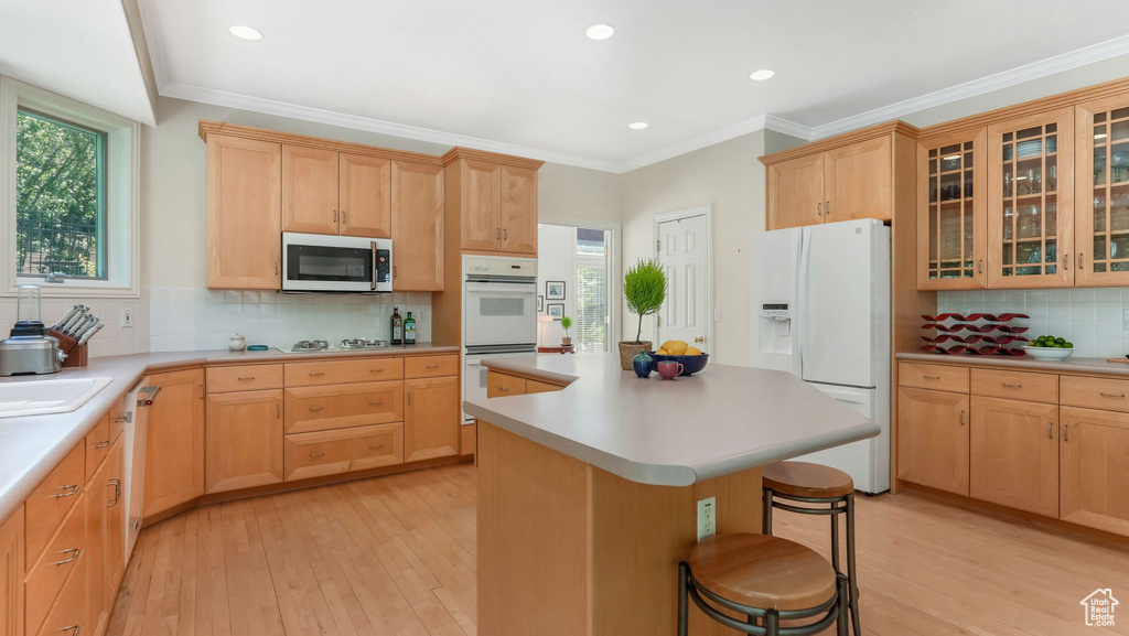 Kitchen with white appliances, light brown cabinetry, light wood-style floors, a breakfast bar, and recessed lighting