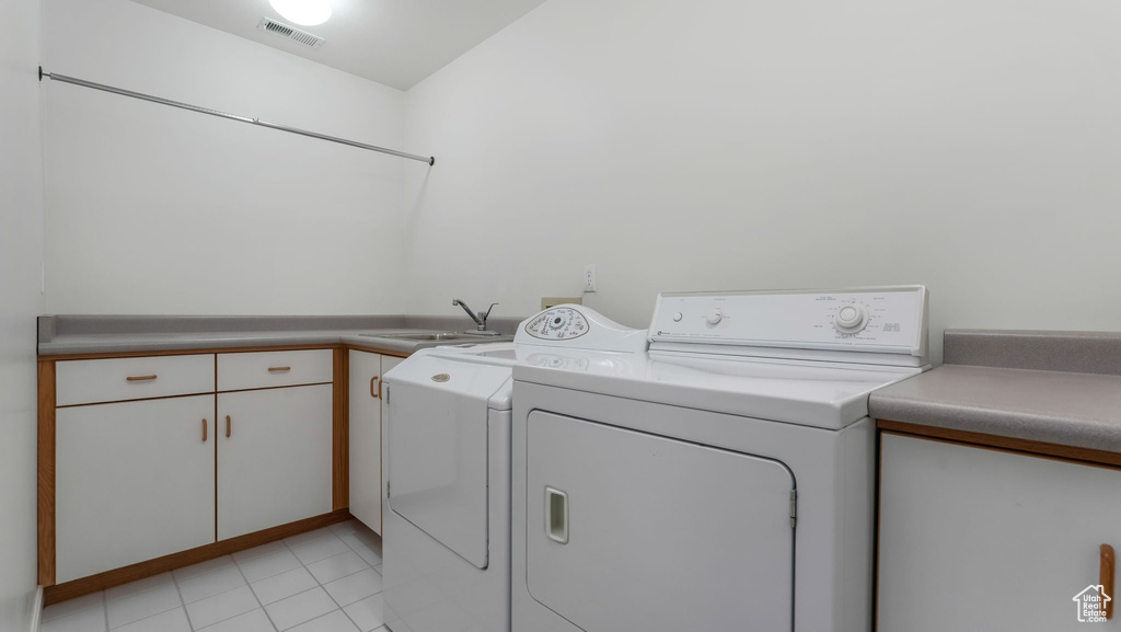 Laundry area with separate washer and dryer, cabinet space, and light tile patterned floors