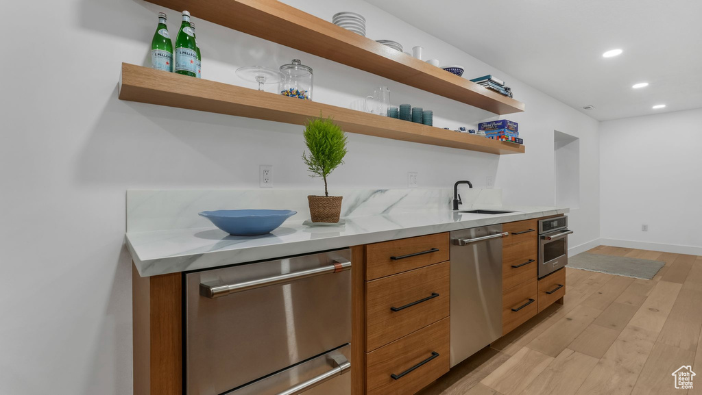 Kitchen with open shelves, stainless steel appliances, modern cabinets, a sink, and light wood-style flooring