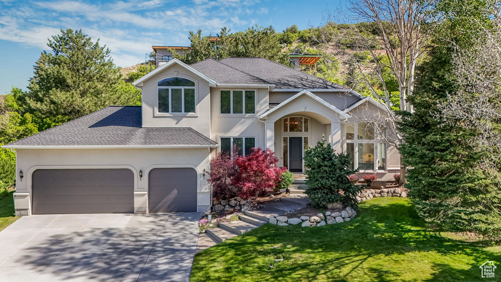 Traditional home featuring stucco siding, driveway, a garage, and roof with shingles