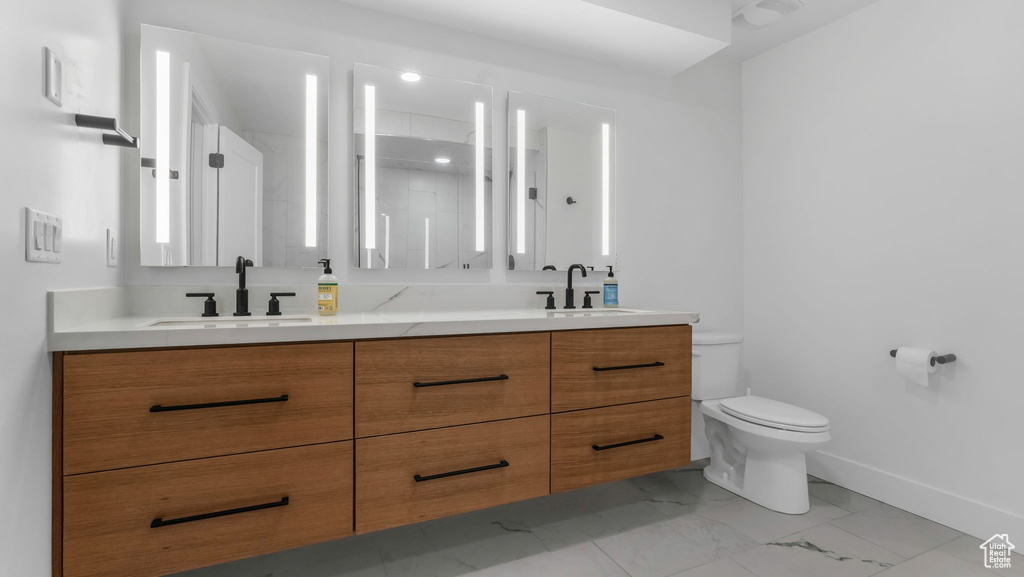 Bathroom featuring double vanity, toilet, marble look tile flooring, and baseboards