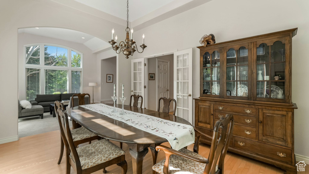 Dining room with arched walkways, a chandelier, lofted ceiling, light wood finished floors, and baseboards
