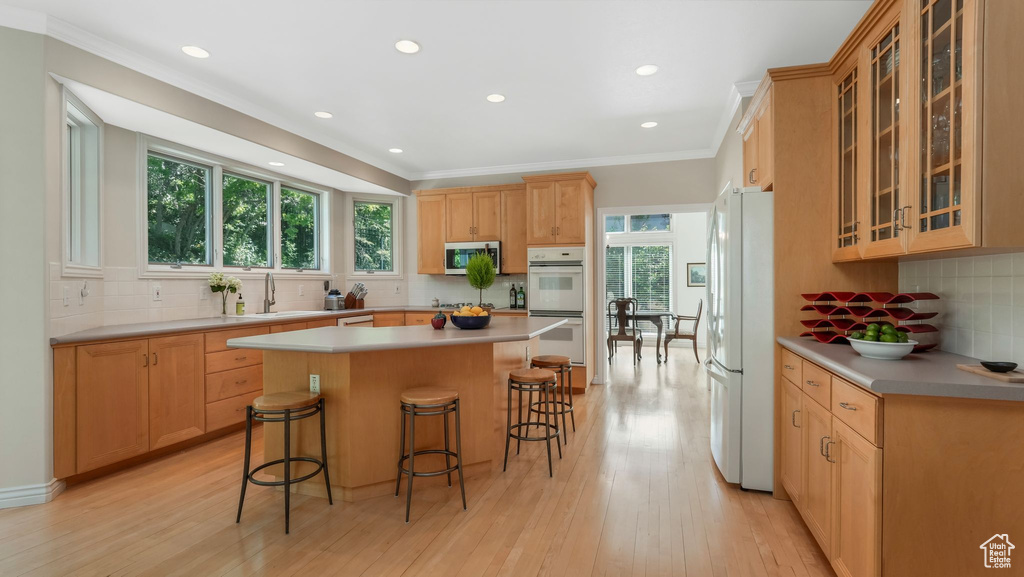 Kitchen featuring white appliances, tasteful backsplash, a breakfast bar, light wood-type flooring, and ornamental molding
